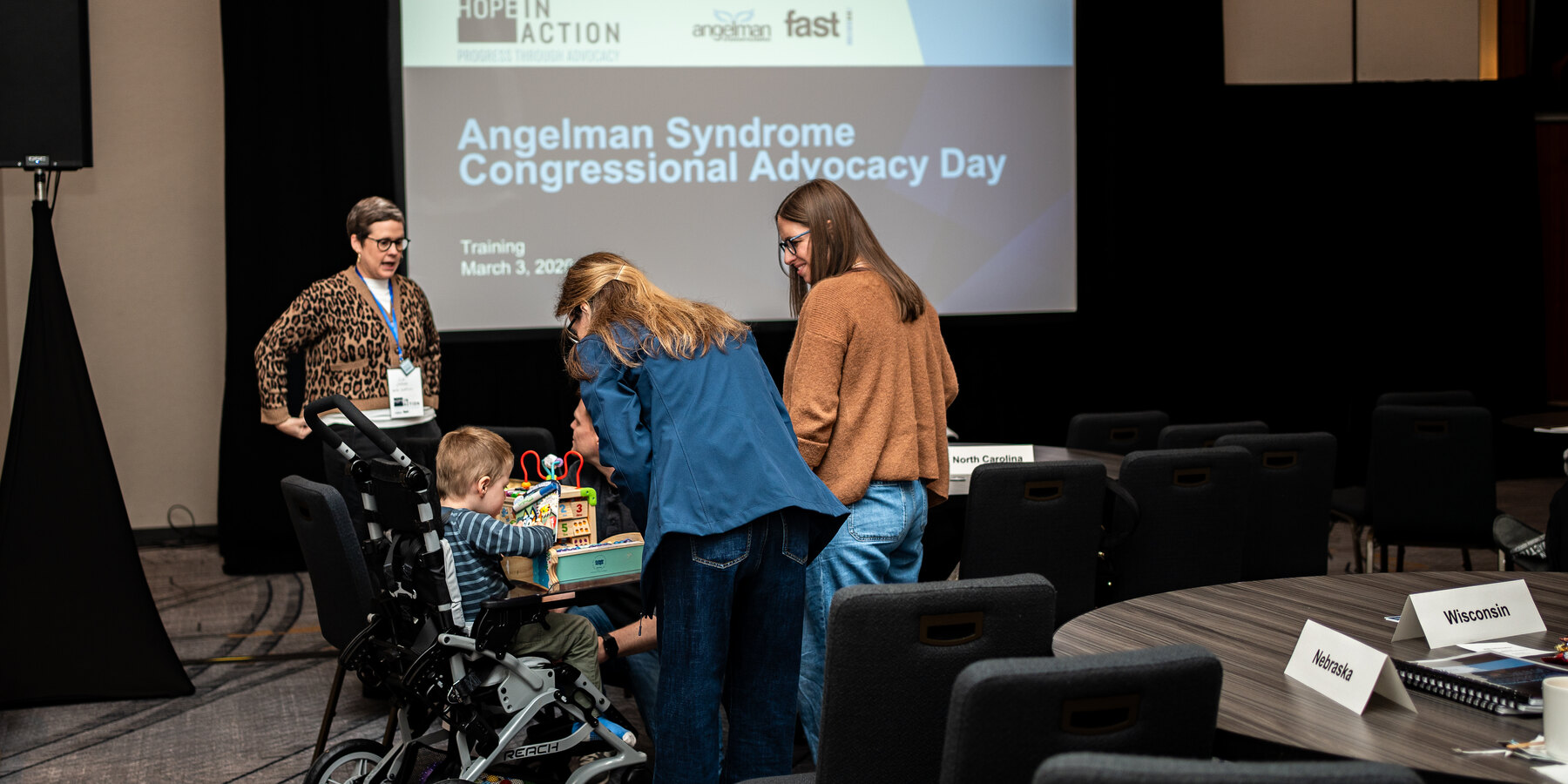 A family with a child in a wheelchair in front of the Hope in Action screen at the advocacy meeting