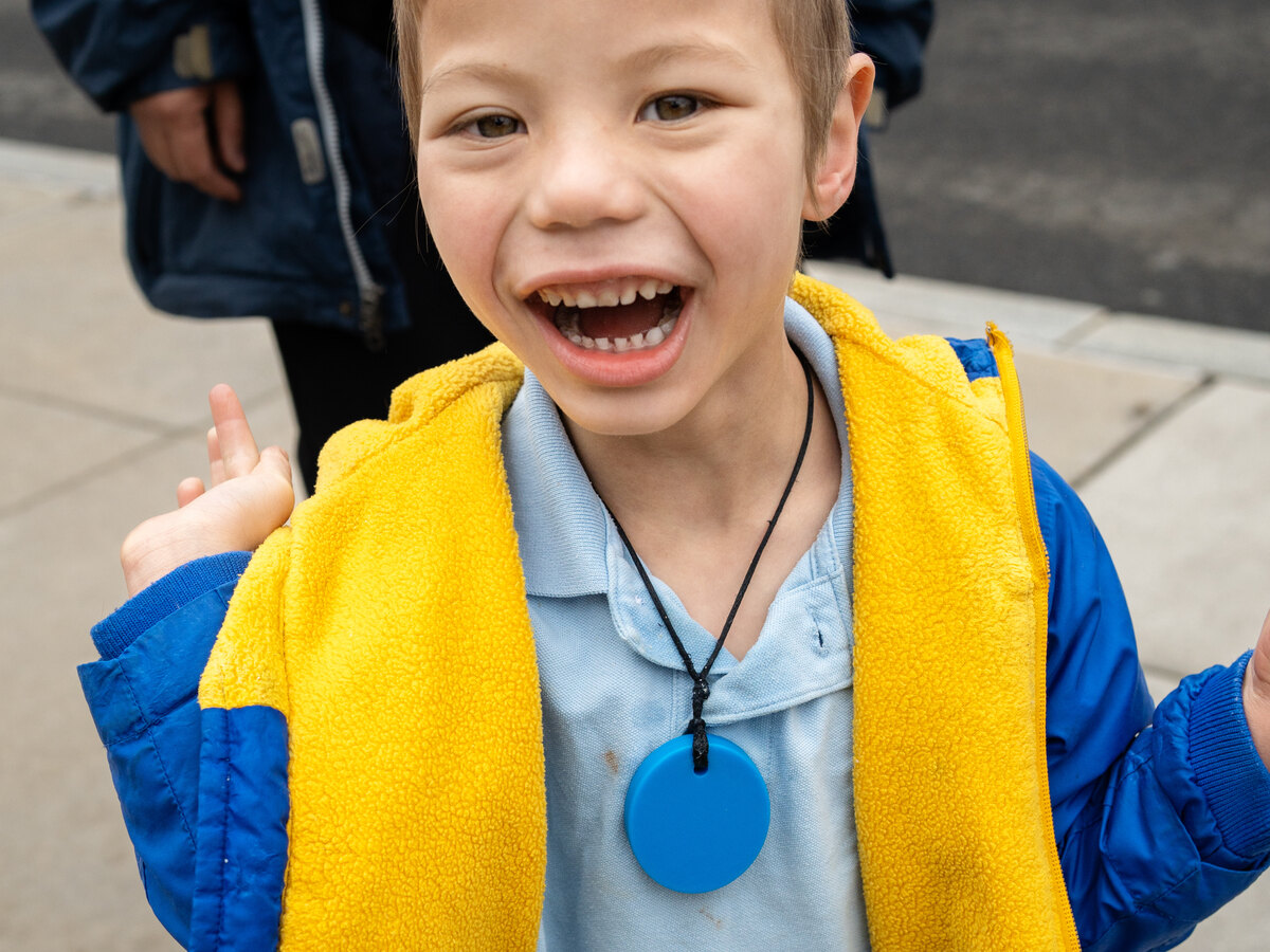 A boy with Angelman syndrome waving, wearing a blue and yellow jacket