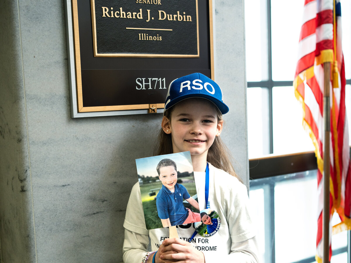 A young sibling advocate holding a photo of a child with Angelman syndrome outside a US Senate office